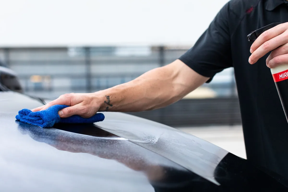 Detailer hand-finishing a panel with microfiber and spray - the finished work a converting detailing website has to showcase