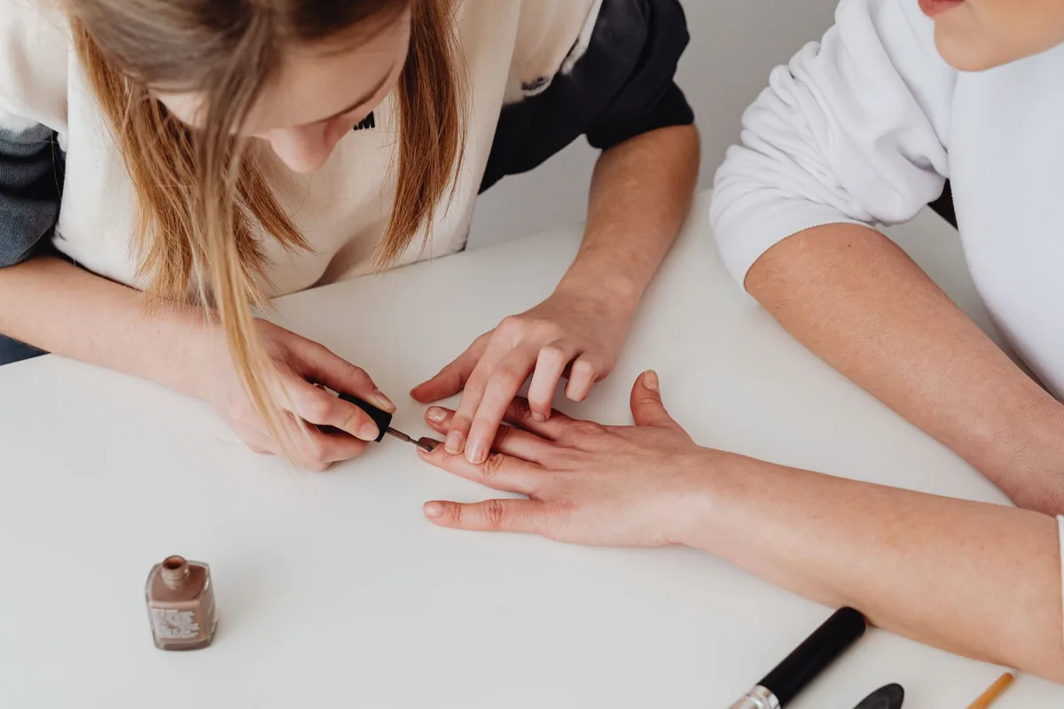 Nail technician painting a client's nails during a salon appointment secured with a booking deposit